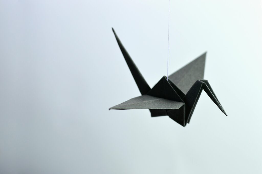 A minimalist black origami crane elegantly suspended against a soft background.