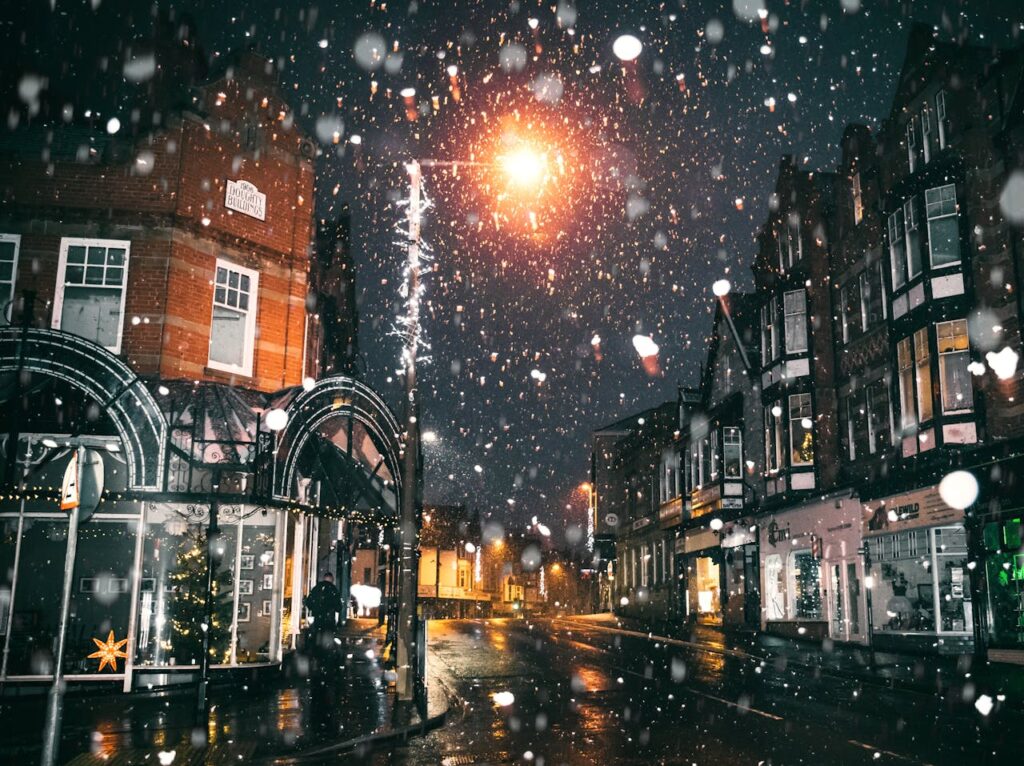 a snowy street with a lit light pole and buildings exemplifying wintertime